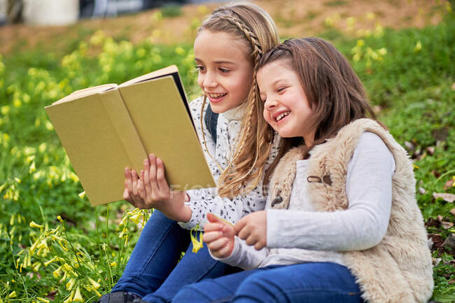 Розумні діти сидять на зеленому пагорбі в парку і читають цікаві книжки під час вихідних. — стокове фото