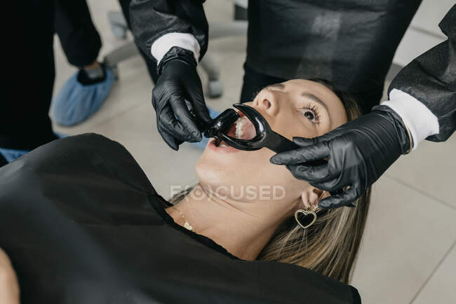 Grand angle de culture dentiste méconnaissable avec rétracteurs examinant les dents de la cliente pendant le traitement dentaire en clinique contemporaine — Photo de stock