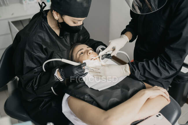Desde arriba de los dentistas con taladro dental y jeringa de agua de aire haciendo tratamiento de dientes para el cliente en la clínica moderna - foto de stock