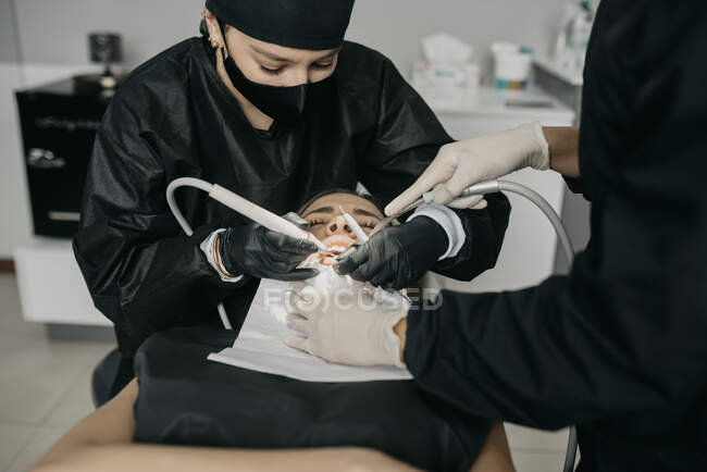 From above of dentists with dental drill and air water syringe making treatment of teeth for client in modern clinic — Stock Photo