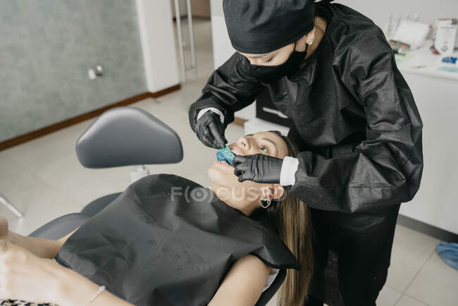 Dentiste avec moule pour les dents de la cliente pendant le traitement dentaire dans une clinique contemporaine — Photo de stock