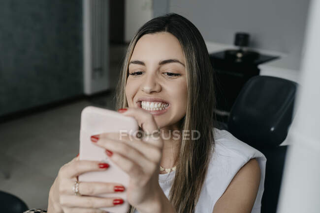 Patiente aux dents blanches assise sur une chaise dentaire et autoportant sur smartphone après traitement en clinique — Photo de stock