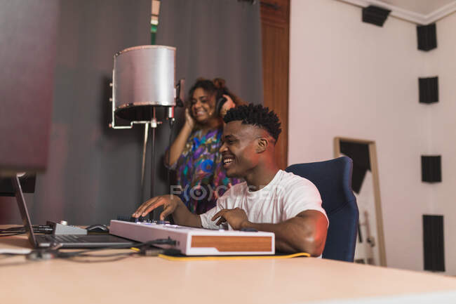 Vista lateral de los jóvenes socios afroamericanos utilizando netbook con software de grabación de sonido en la pantalla en el estudio de música - foto de stock