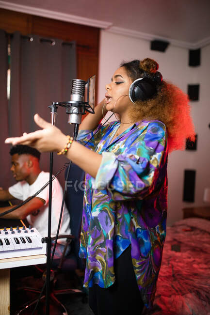 Сторона зору молодого афроамериканського вокаліста в навушниках записує пісню проти посміхаючись музичного продюсера в студії — стокове фото