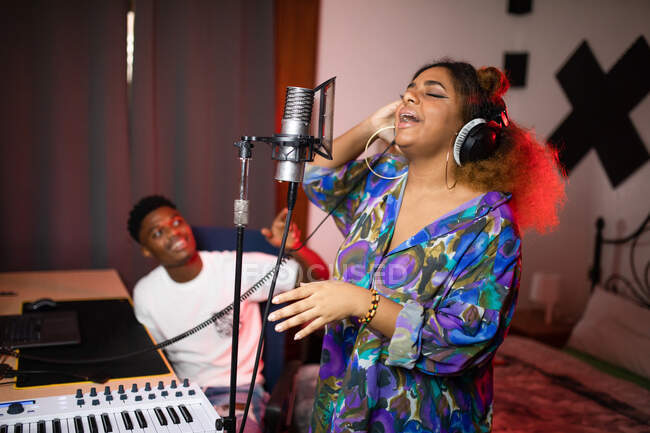 Сторона зору молодого афроамериканського вокаліста в навушниках записує пісню проти посміхаючись музичного продюсера в студії — стокове фото