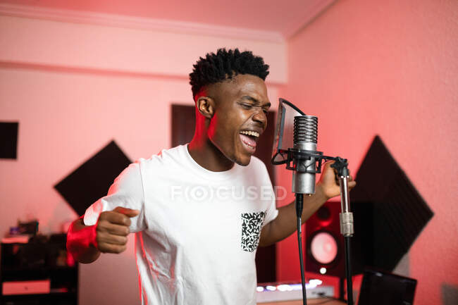 Young African American vocalist with open mouth and modern haircut singing into professional mic — Stock Photo