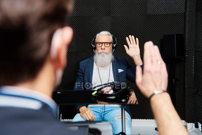 Пожилой бородатый мужчина в наушниках сидит в звукоизолированной комнате во время аудиологического осмотра и теста на слух — стоковое фото