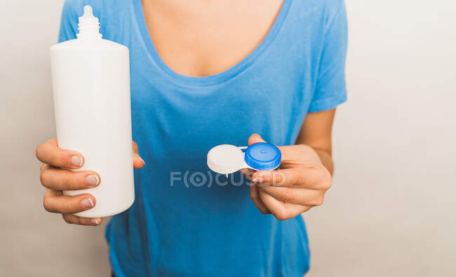 Crop mujer anónima con camisa azul casual que muestra un paquete reutilizable de plástico con lentes de contacto contemporáneas y botella con solución - foto de stock