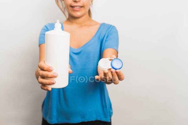 Crop anonyme femelle portant une chemise bleue décontractée montrant un paquet réutilisable en plastique avec des lentilles de contact contemporaines et une bouteille avec solution — Photo de stock