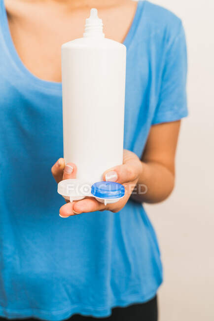 Анонімні жінки, які носять повсякденну синю сорочку, показують пластиковий багаторазовий пакет з сучасними контактними лінзами та пляшкою з розчином — стокове фото