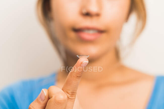 Crop borrosa hembra sonriente preparándose para poner en lente de contacto en la punta del dedo en la sala de luz - foto de stock