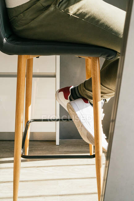 Bein der Ernte unkenntlich Männchen in Turnschuhen sitzt auf Hocker zu Hause — Stockfoto