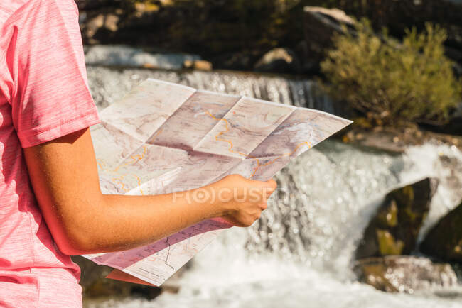 Donna viaggiatore irriconoscibile in piedi con mappa cartacea vicino alla cascata nel Parco Nazionale di Ordesa y Monte Perdido e orientarsi durante le vacanze in montagna Pirenei — Foto stock