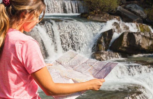 Side view of traveling woman standing with paper map near waterfall in Ordesa y Monte Perdido National Park and orientating during vacation in Pyrenees mountains — Stock Photo