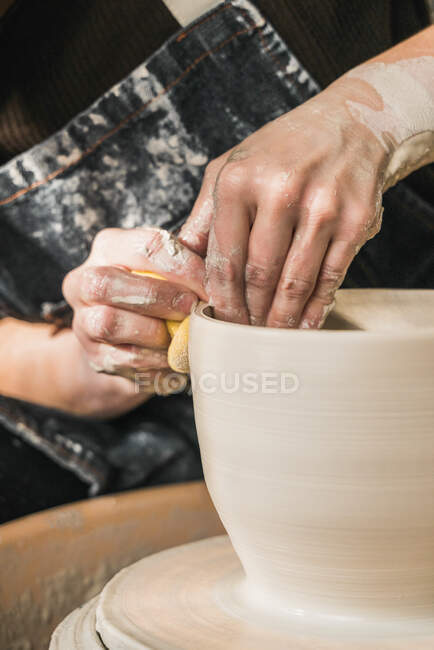 Artesana anónima recortada usando rueda de cerámica y creando artículos de barro hechos a mano en el taller - foto de stock