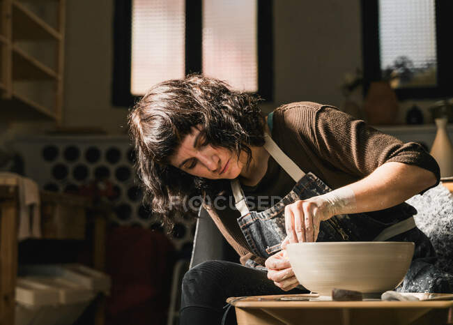 Фокусированная женщина-ремесленница с помощью гончарного колеса и создание ручной глиняной посуды в мастерской — стоковое фото