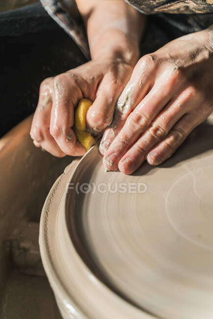 De arriba de la cosecha la artesana irreconocible que crea la loza sobre la rueda de cerámica en el estudio - foto de stock