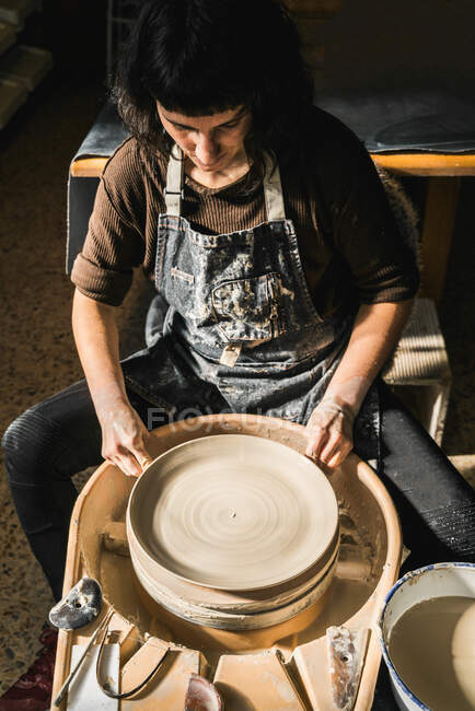 Сверху сосредоточены женщины-ремесленницы с помощью гончарного колеса и создание ручной глиняной посуды в мастерской — стоковое фото