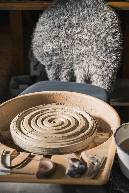 Schmutzige Töpferscheibe und Ton mit Stuhl in kreativer Werkstatt des Kunsthandwerkers platziert — Stockfoto