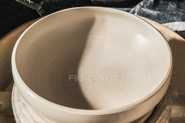 Desde arriba de simple cuenco de cerámica hecho a mano en la rueda de cerámica colocado en el taller creativo - foto de stock