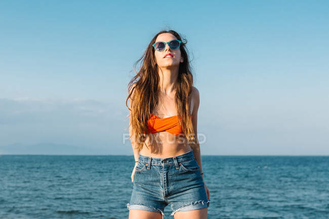 Впевнена довготривала хіпстерська жінка-підліток у стильному літньому вбранні та сонцезахисних окулярах, насолоджуючись літнім відпочинком на узбережжі — стокове фото