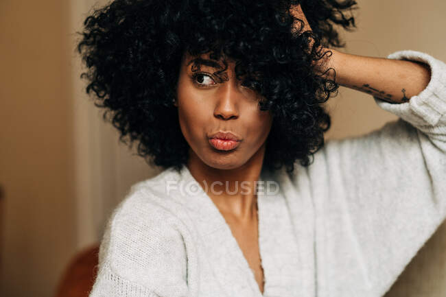 Довірлива афро-американська жінка з кучерявим волоссям сидить на дивані торкаючись волосся, дивлячись у далечінь додому — стокове фото
