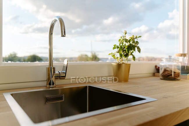 Square sink on wooden counter top located near window in modern kitchen on sunny day — Stock Photo