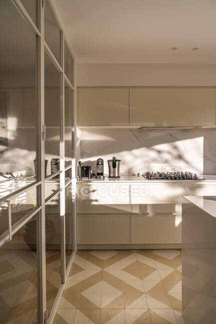 Интерьер современной домашней кухни с легкой мебелью и зеркальными элементами при дневном свете — стоковое фото