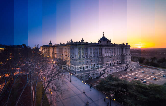 Old magnificent building facade against parked vehicles under colorful sky with sun in evening in Madrid — Stock Photo