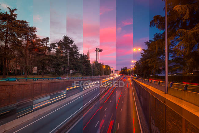 Asphalt roadways with driving vehicles between high trees under bright cloudy sky in town at sundown — Stock Photo