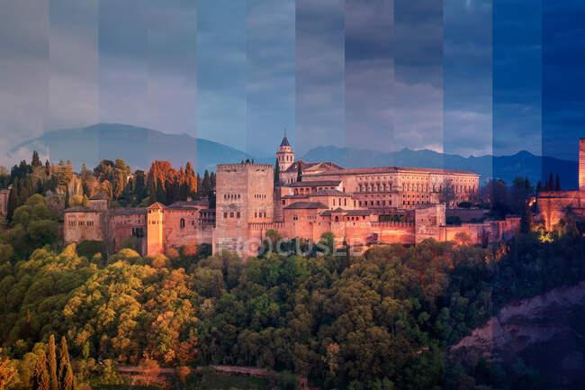 Antiguo palacio de piedra y fachada de fortaleza entre árboles verdes contra montañas en el crepúsculo en Granada España - foto de stock