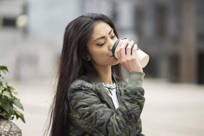 Молода азіатка в стильному одязі насолоджується кавою на вихідних у парку. — стокове фото