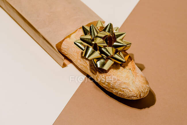 Minimalistic still life composition with fresh artisan bread loaf in paper package with golden gift bow on table — Stock Photo