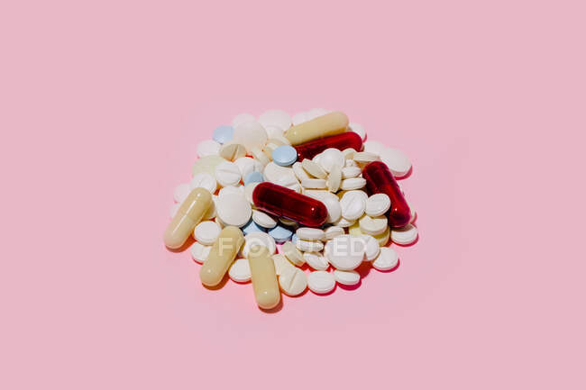 Куча разноцветных капсул и таблеток разных размеров, размещенных на розовом фоне — стоковое фото