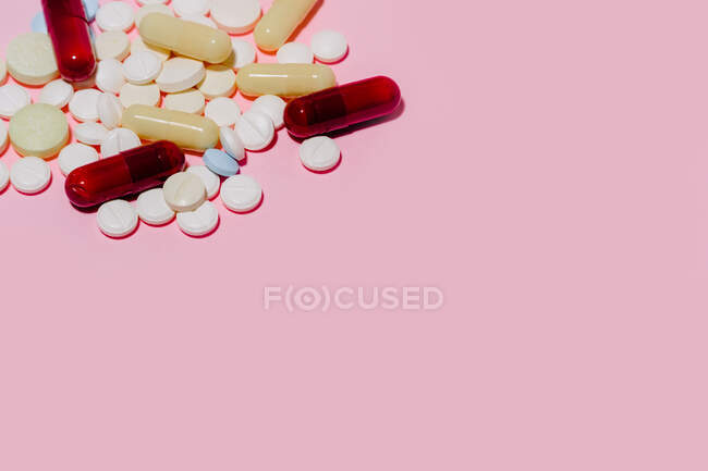 Купа різних різнокольорових капсул і таблеток різного розміру розміщені на рожевому фоні. — стокове фото