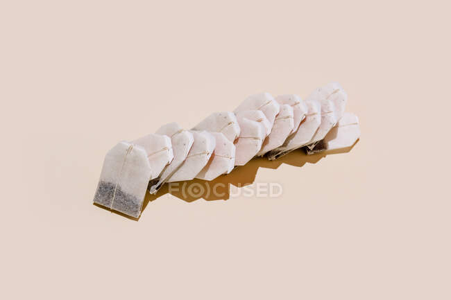 From above of paper tea bags arranged in row on beige background with empty space — Stock Photo