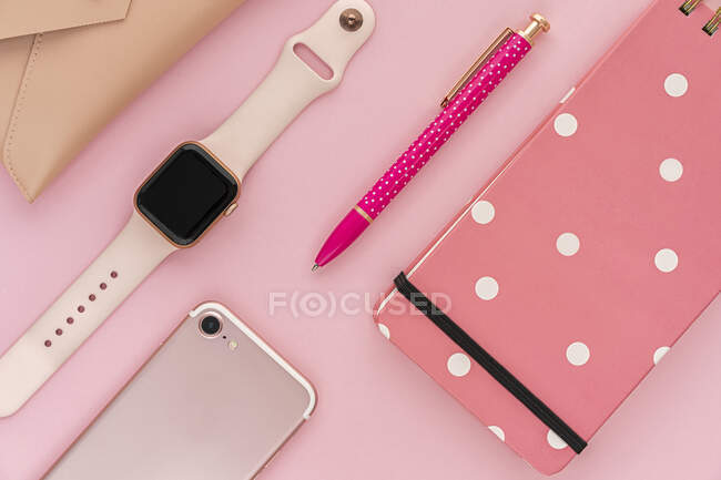 Vista superior plana composición laica con estiloso bolígrafo rosa y moderno reloj de pulsera femenino arreglado con teléfono inteligente y portátil en el escritorio - foto de stock
