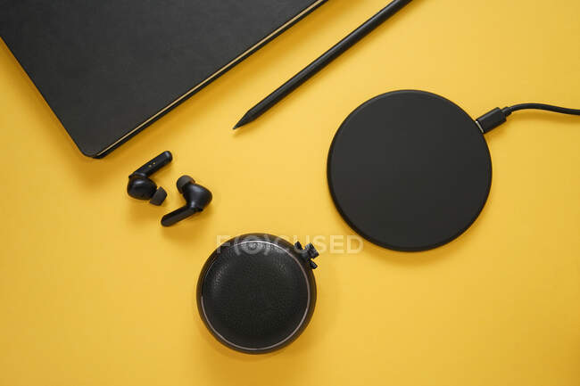 Композиція зверху з чорними справжніми бездротовими навушниками поблизу корпусу, розміщеними на жовтому столі з зарядкою та планшетом зі стилусною ручкою — стокове фото