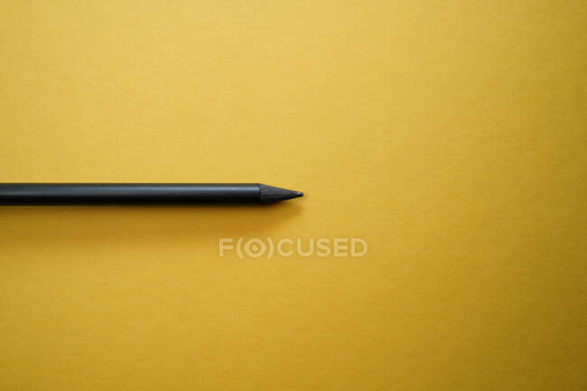 Вид зверху мінімалістична композиція з чорним олівцем, розташованим на жовтому тлі з порожнім простором — стокове фото