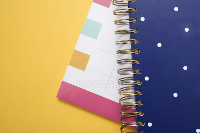 Composición de vista superior con calendario de planificador multicolor y cuaderno espiral azul apilado sobre fondo amarillo - foto de stock