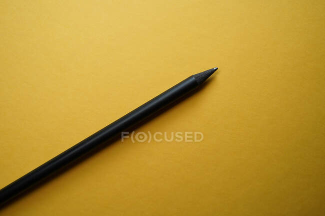 Вид зверху мінімалістична композиція з чорним олівцем, розташованим на жовтому тлі з порожнім простором — стокове фото