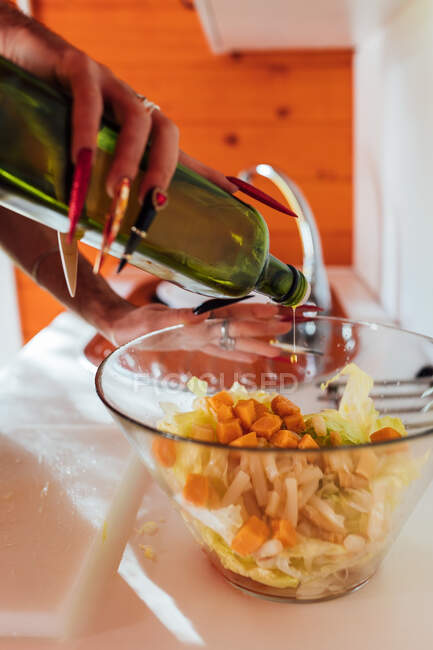 Cultivo cozinheiro anônimo com manicure adicionando azeite à salada de legumes em tigela na cozinha — Fotografia de Stock