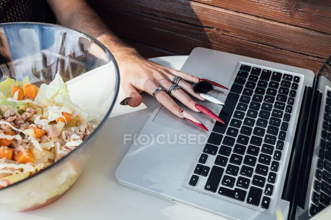 Cropped unrecognizable transgender man surfing internet on netbook at table with food against bungalow — Stock Photo