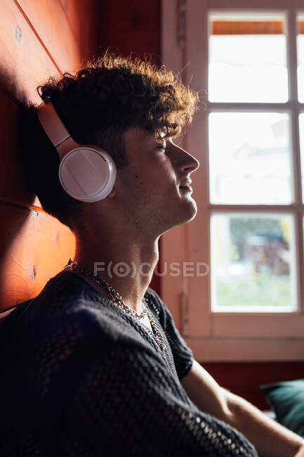 Вид сбоку молодого заботливого мужчины с закрытыми глазами, слушающего песню из беспроводной гарнитуры в салоне — стоковое фото