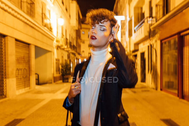 Young trendy transgender male standing on urban pavement with eyes closed in twilight — Stock Photo