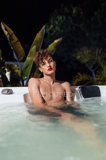 Молодий транссексуал з довгими цвяхами дивиться на камеру, що лежить у гарячій ванні в сутінках — стокове фото
