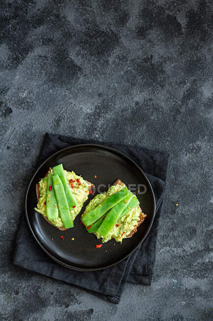 Appetizing toasts with fresh guacamole and green peas pods garnished served on black plate — Stock Photo