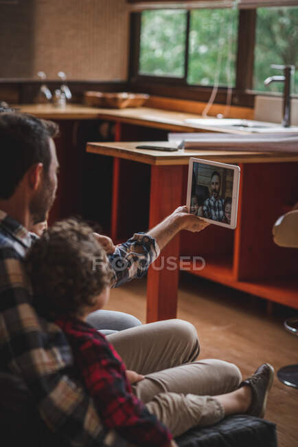 Vista lateral do pai amoroso sentado no sofá com crianças e tomando selfie no comprimido juntos — Fotografia de Stock