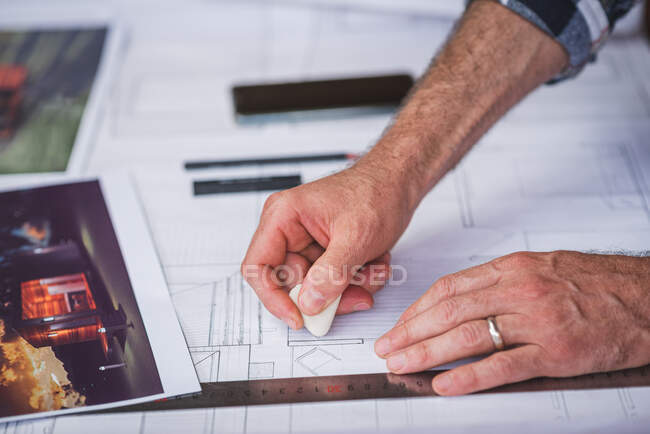 Crop unrecognizable male architect creating draft of building and erasing lines while working on project at home — Stock Photo