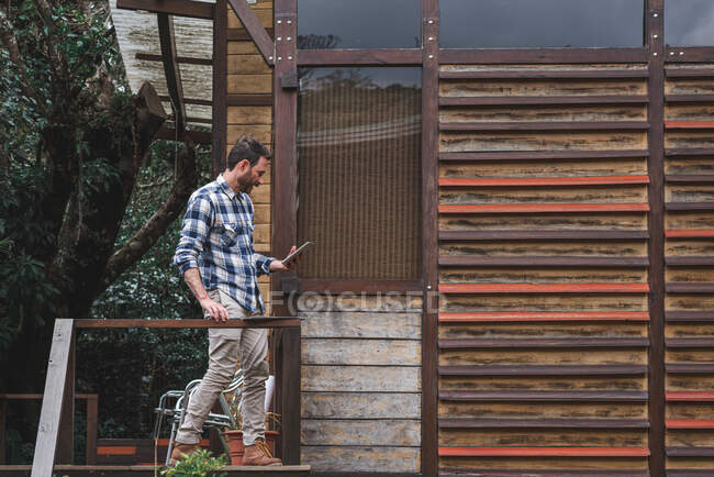 Vista lateral do arquiteto masculino ocupado em pé no terraço com planta e tablet de navegação enquanto trabalha no projeto — Fotografia de Stock